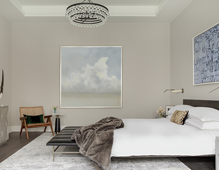 View of a modern master bedroom with low king sized bed, modern artowrk on the wall and a brown leather chari in the corner in Houston, TX